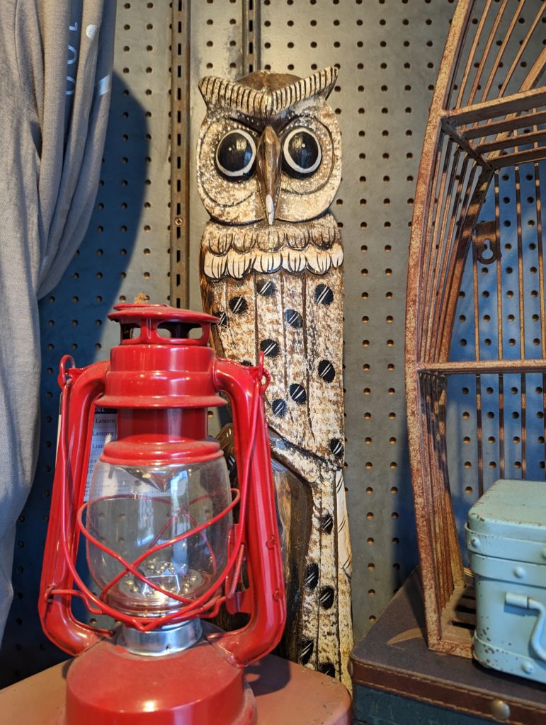 A tall, think sculpture of a beige own behind an old, red kerosene lantern.