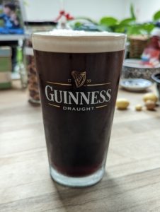 A closeup of a pint glass full of Guinness a dark stout with a light foamy top. 