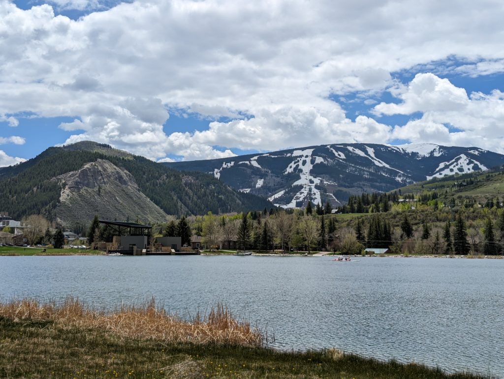 A wide shot with a still snow covered beaver creek ask resort in the background and a spring time lake in the foreground.