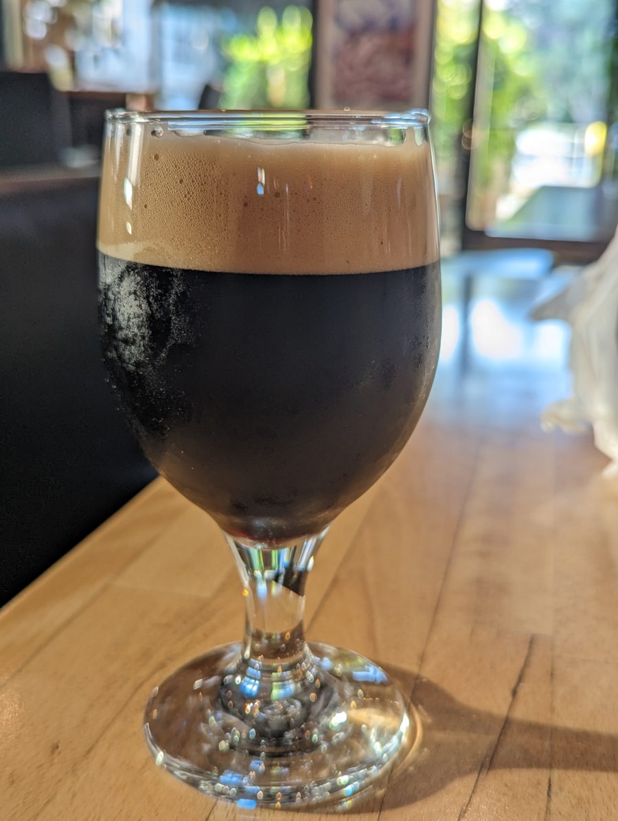 A goblet of stout beer. The upper fourth is a rich creamy light brown head atop the black black beer.