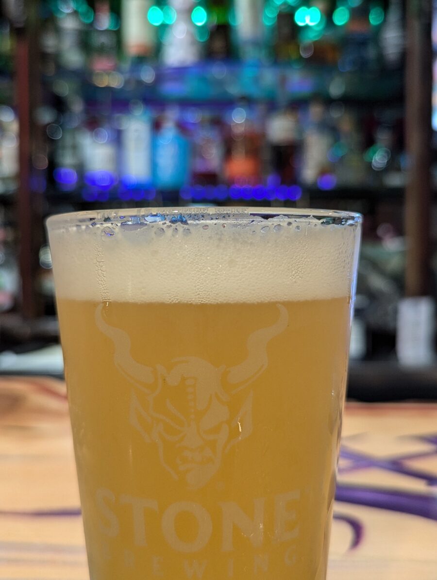 A frosty pint of Hazy IPA in front of shelves full ot liquor behind the bar