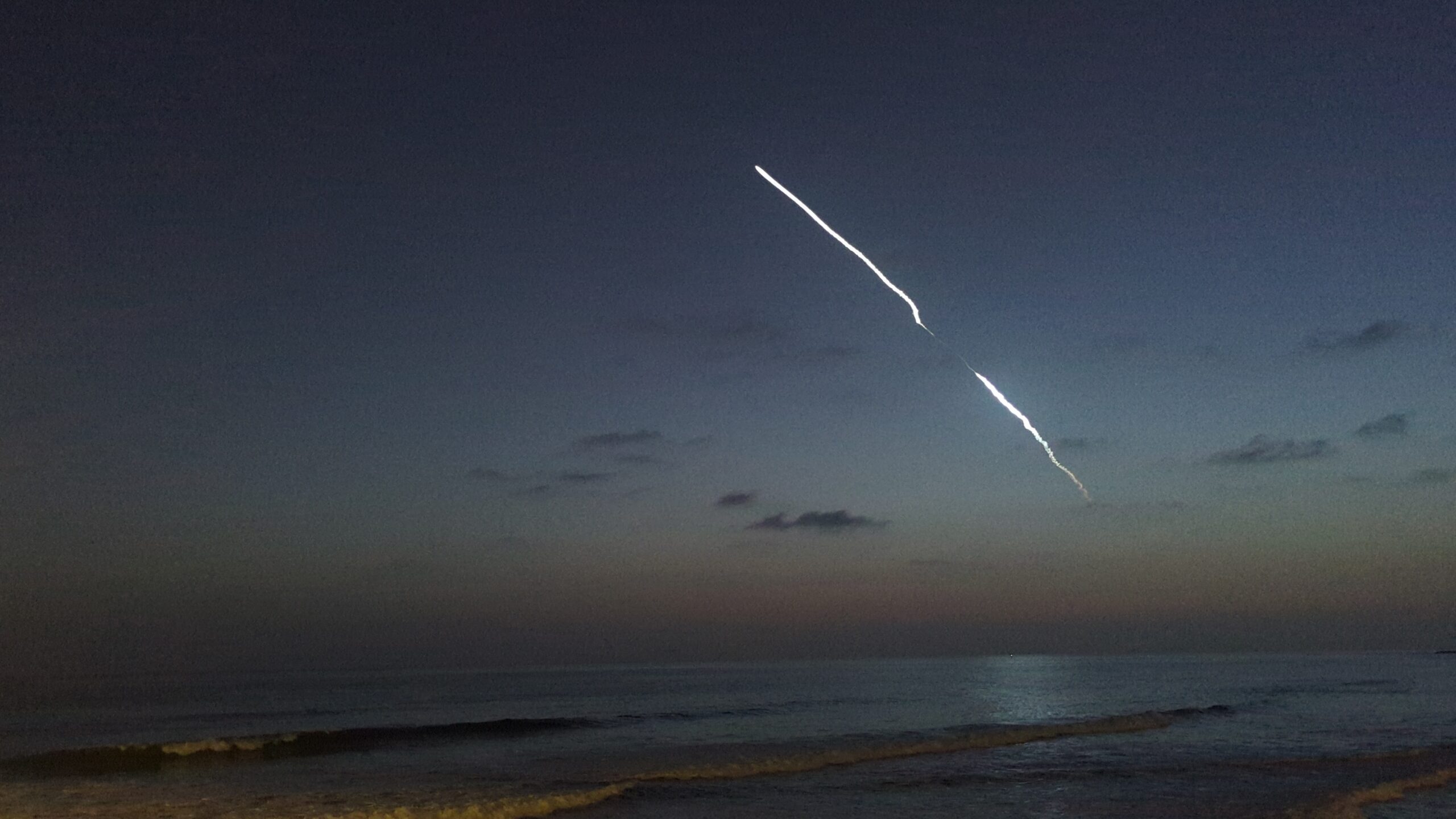 A photograph of a SpaceX Falcon 9 launching over the Pacific Ocean