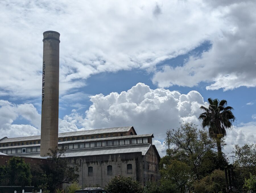 A photography of the Brewery smokestack shortly after a rain. There are big billowy clouds in the sky behind a slightly rain soaked industrial building.