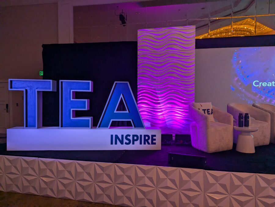 A photograph of a stage in the Sheraton Universal ballroom with a large TEA Inspire stand up logo.