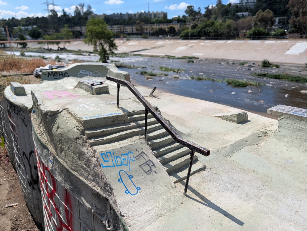 A photo of a mini skate park, built for finger boards, installed next to the LA River. This photo features tiny stairs and a railing.